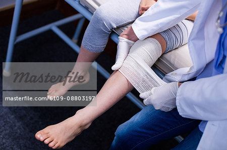 Doctor putting bandage on injured leg of patient in hospital