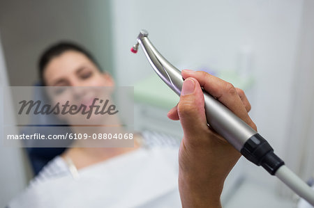 Close-up of dentist holding a dentistry, dental handpiece while examining a woman at clinic