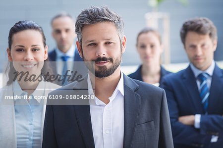 Portrait of confident businessman with colleagues standing outside office building