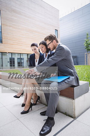 Businesswoman sitting with colleagues and using laptop outside office building