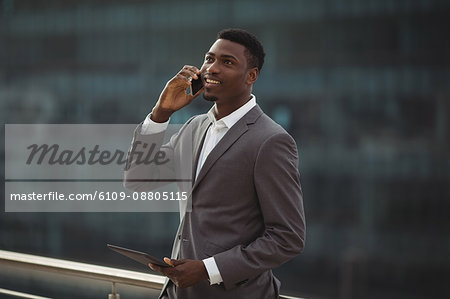 Businessman holding digital tablet and talking on mobile phone on office terrace