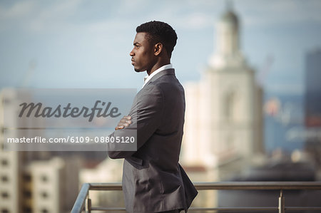 Side view of businessman standing with arms crossed on office terrace