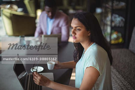 Thoughtful businesswoman holding coffee cup sitting at her desk in office