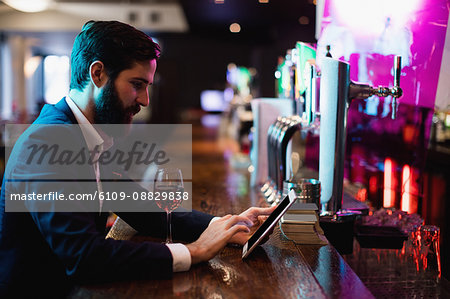 Businessman using digital tablet with wine glass on counter