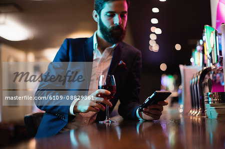 Businessman using mobile phone with glass of red wine in hand