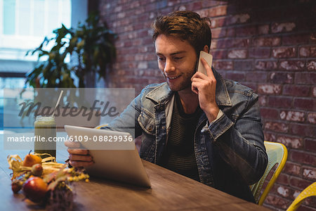 Man talking on mobile phone while using digital tablet