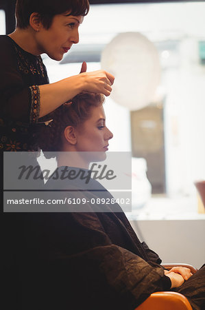 Female hairdresser styling clients hair in saloon