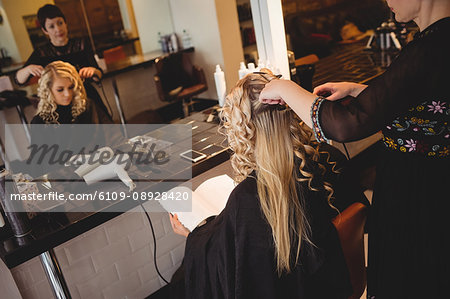 Female hairdresser styling clients hair in saloon