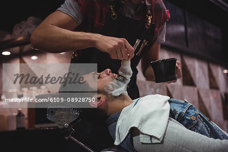 Mid section of barber applying cream on clients beard in baber shop