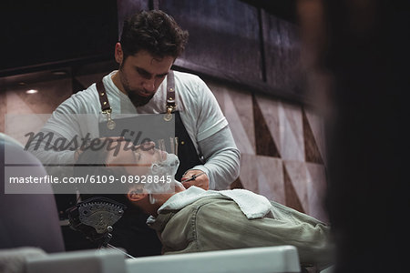 Man getting his beard shaved with razor in barber shop