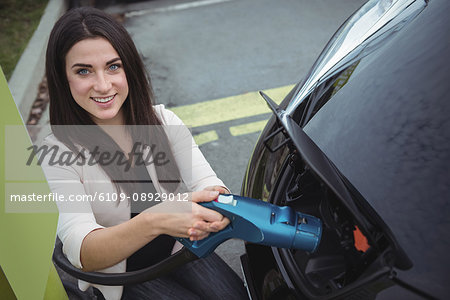 Portrait of beautiful woman charging electric car on street