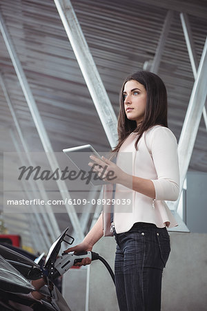 Beautiful woman using digital tablet while charging electric car at vehicle charging station