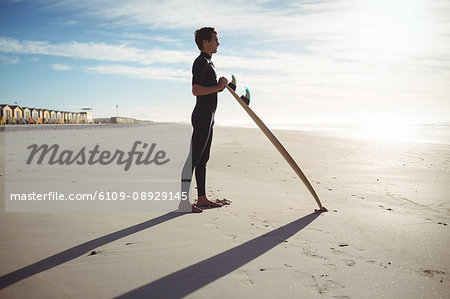 Thoughtful surfer standing with surfboard on beach