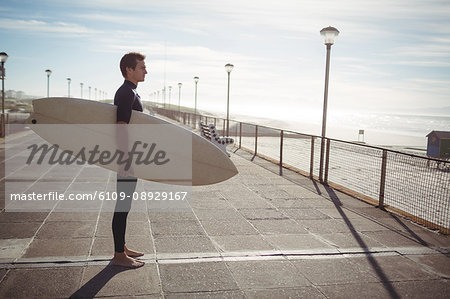 Thoughtful surfer standing with surfboard on pier at beach