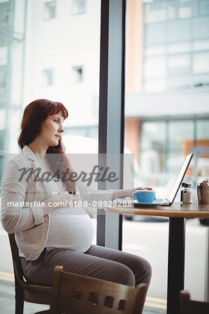 Pregnant businesswoman using laptop in office cafeteria