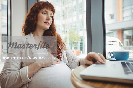 Pregnant businesswoman using laptop in office cafeteria