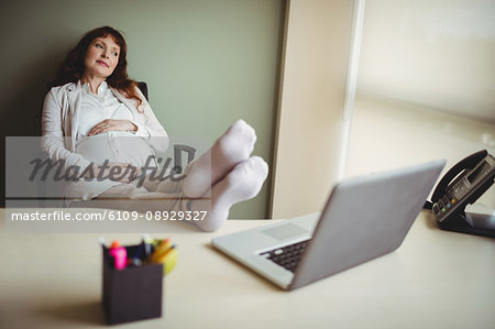 Pregnant businesswoman relaxing with her feet up in office Pregnant businesswoman relaxing with her feet up in office
