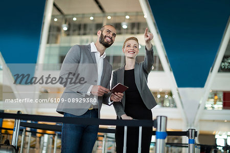 Businesswoman standing with her colleague and pointing at the distance at airport terminal