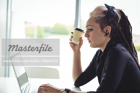 Woman holding disposable coffee cup while using laptop in café
