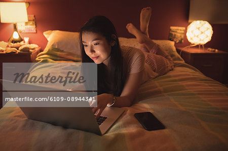 Woman lying and using laptop on bed in bedroom