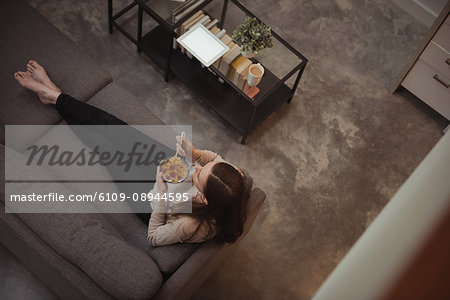 Woman sitting on the sofa and having bowl of bowl of cereals a home