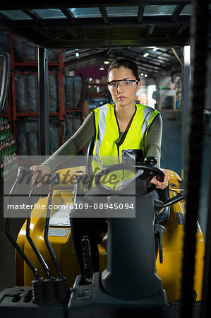 Portrait of confident female worker driving forklift in warehouse