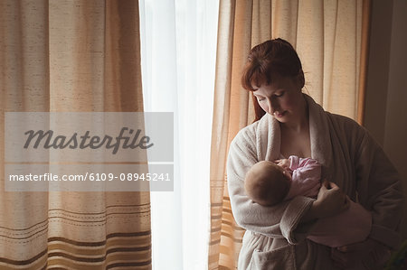 Loving mother with baby standing against curtain at home