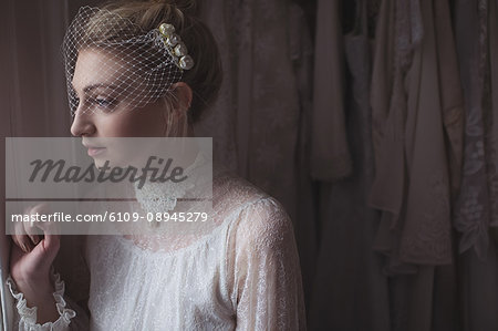 Thoughtful young bride looking through window in a boutique