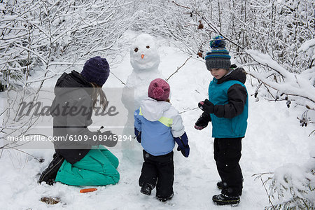 Mother with children making snowman on snowy day