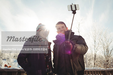 Happy Skier couple clicking a selfie with selfie stick