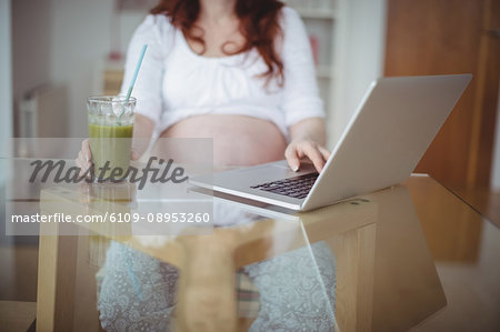 Mid section of pregnant woman using laptop while having juice