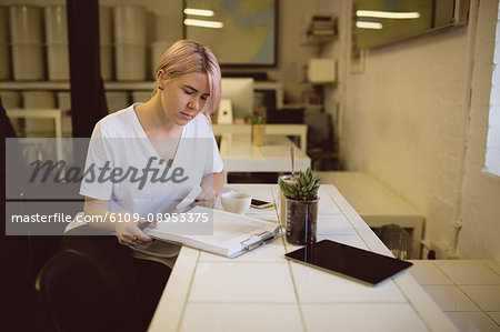 Female barista writing on clipboard while sitting in coffee shop