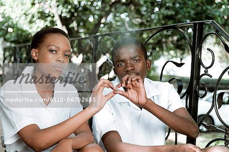 Two African teenagers sit together outside, smoking cigarettes
