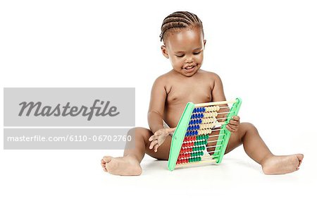 In infant sitting in front of a white background, playing with an abacus