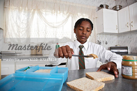 Boy in kitchen spreading peanut butter over bread