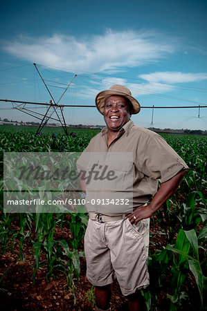 Black farmer stands smiling in a crop field with irrigation systems in the background