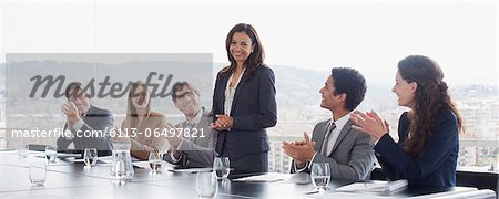 Co-workers clapping for businesswoman in conference room