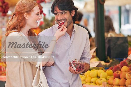 Smiling couple tasting fruit in market