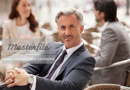 Portrait of smiling businessman at sidewalk cafe with co-workers in background