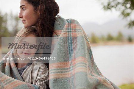 Portrait of smiling daughter wrapped in blanket with mother at lakeside