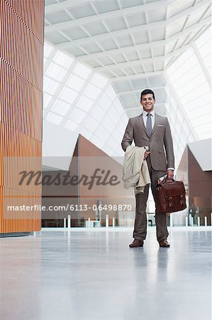 Portrait of smiling businessman holding coat and briefcase in lobby