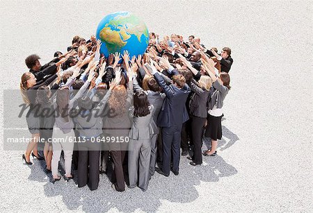 Crowd of business people in huddle reaching for globe