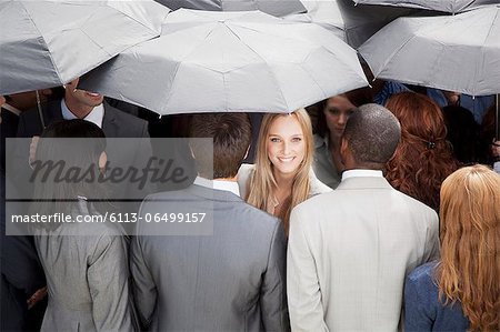 Portrait of smiling businesswoman surrounded by crowd with umbrellas