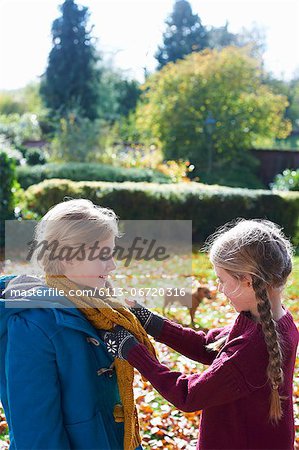 Girl tying sister's scarf outdoors