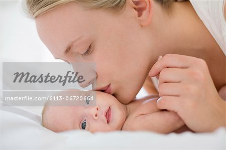 Mother kissing newborn baby on bed