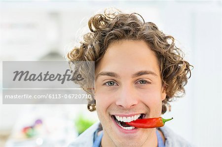 Smiling man holding chili pepper in mouth