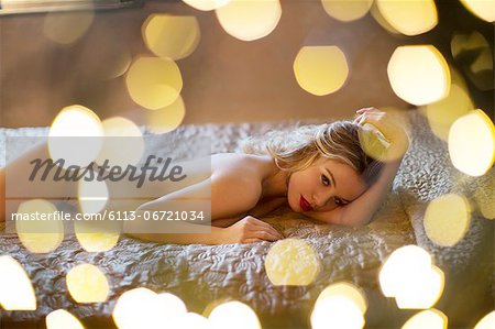 Nude woman surrounded by lights on bed