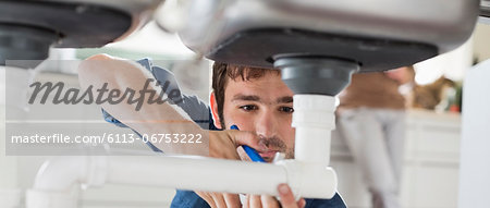 Plumber working on pipes under sink