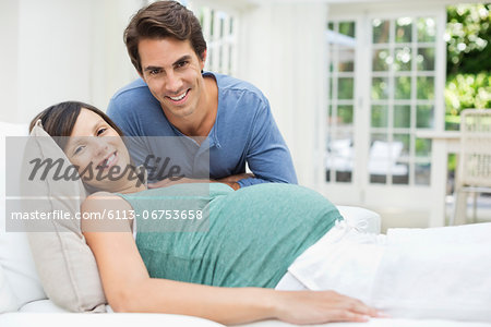 Man sitting next to pregnant woman resting on bed