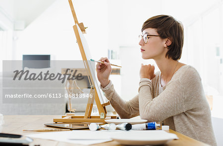 Woman painting on easel at table Woman painting on easel at table